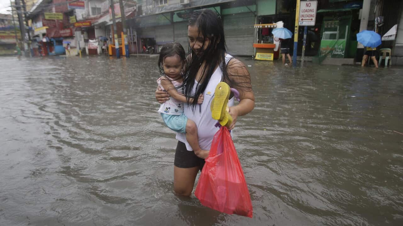 A Filipino woman carries her daughter along a flooded road in suburban Mandaluyong, east of Manila, Philippines.