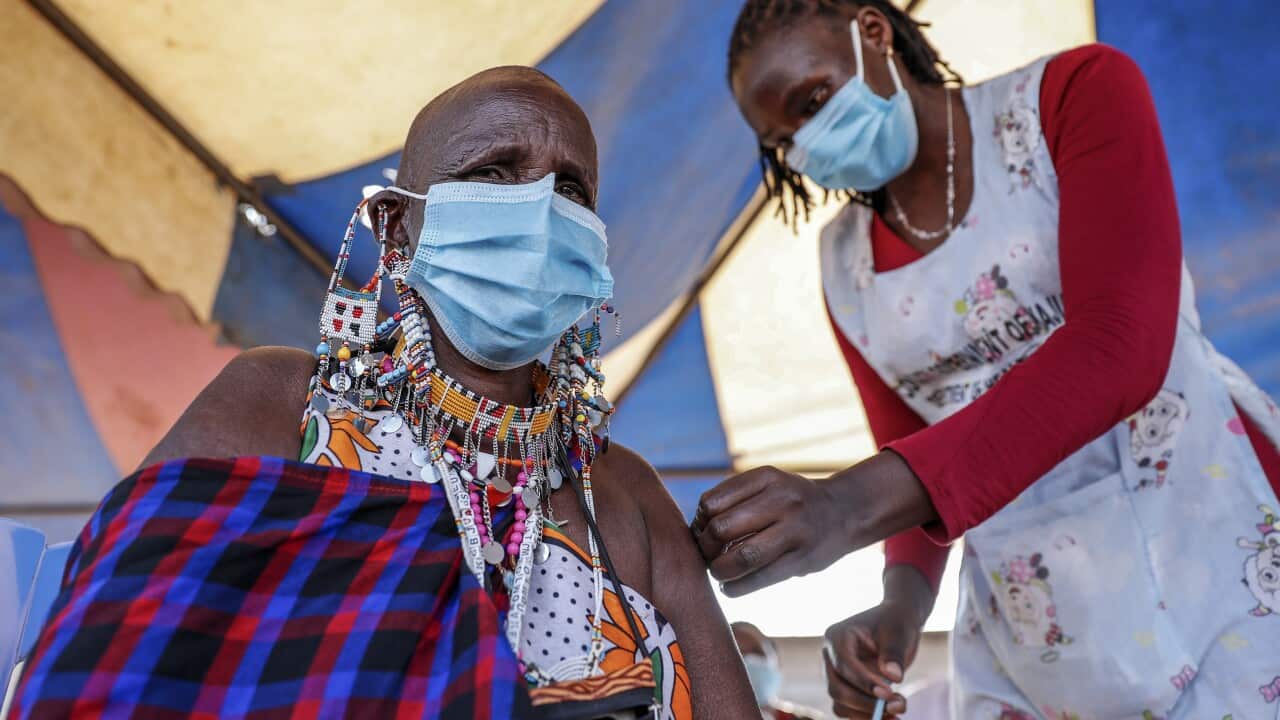 A seated woman receives a vaccine in her arm from a standing health worker.