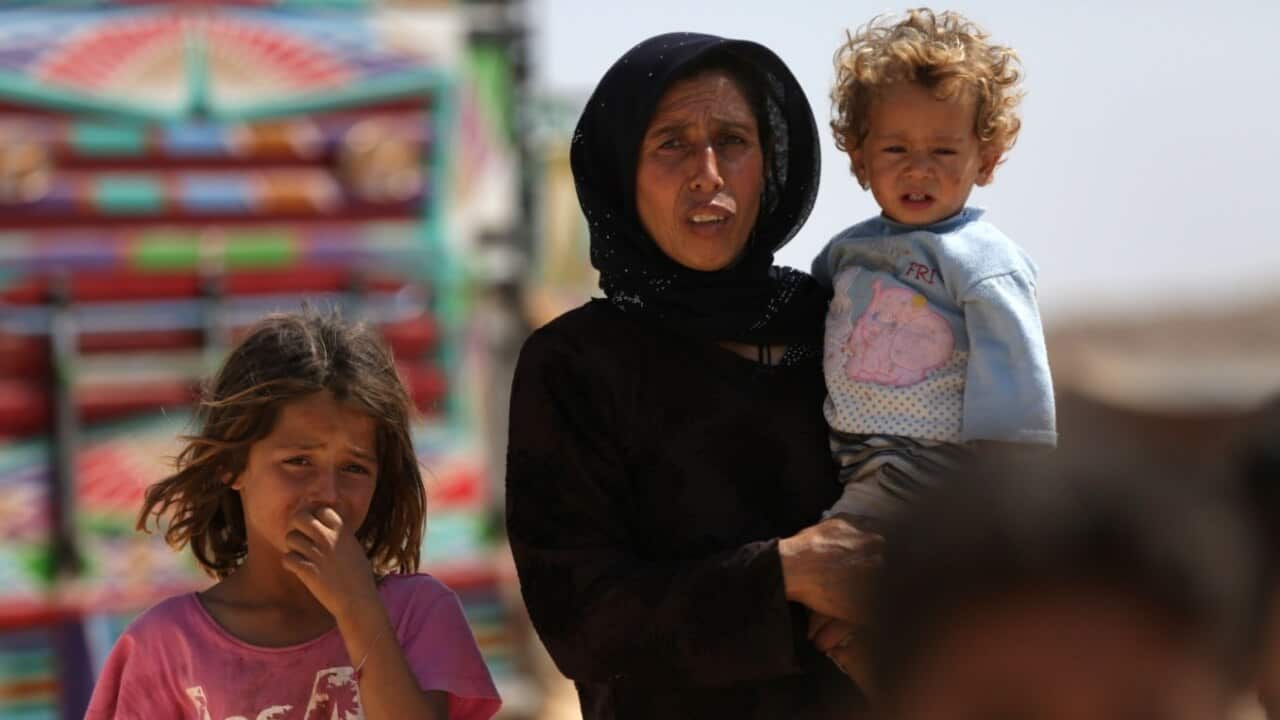 A woman who fled her village in Syria's Idlib province carries a child at a camp in Kafr Lusin near the border with Turkey