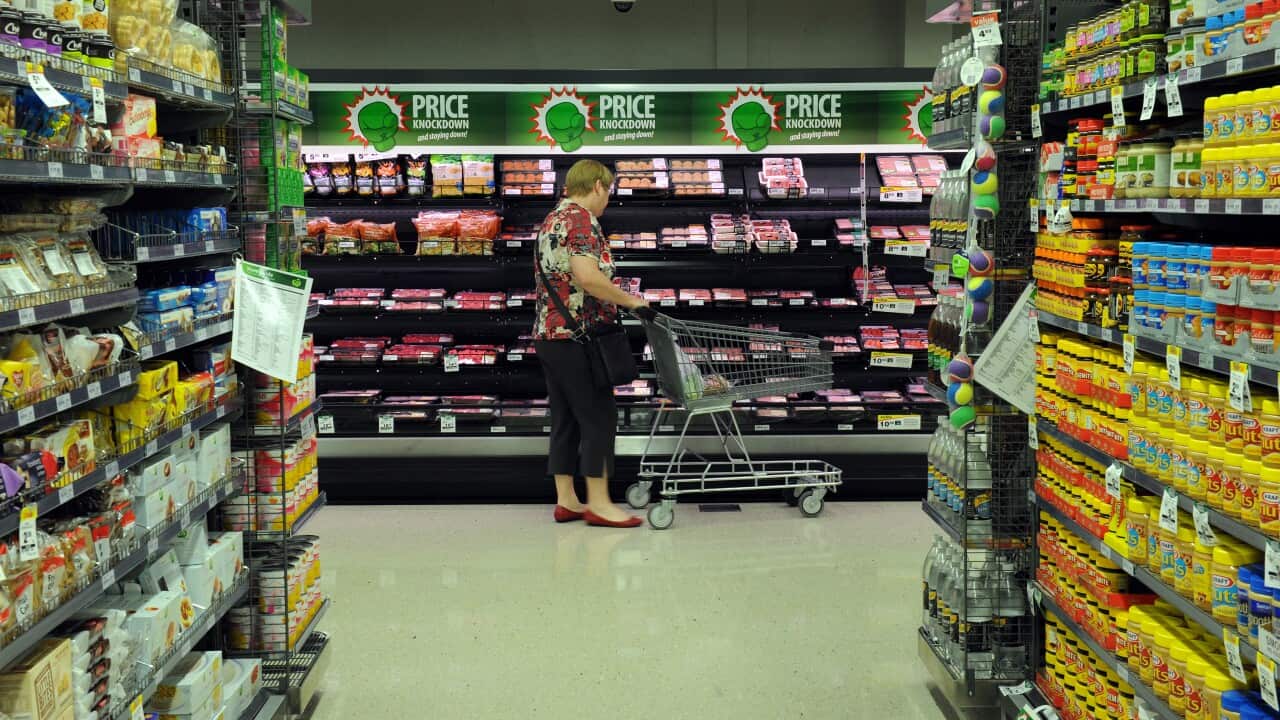 A woman pushes a trolley through a supermarket.
