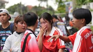 A girl wearing a red shirt cries with other people around her.