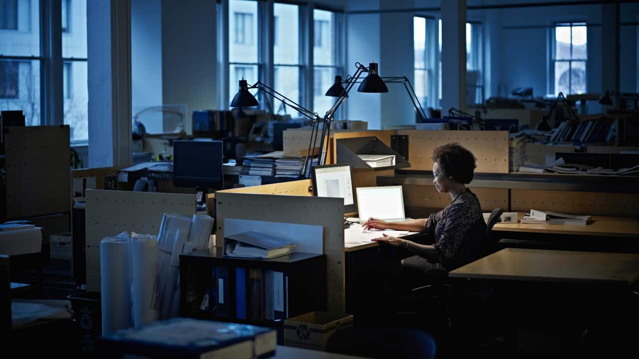 Woman examining documents at desk in an otherwise empty office at night.