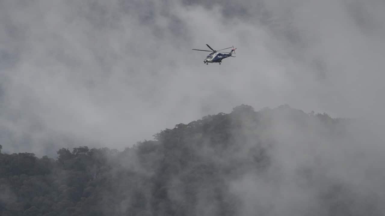 A police helicopter hovers above a misty, tree-covered mountain range.
