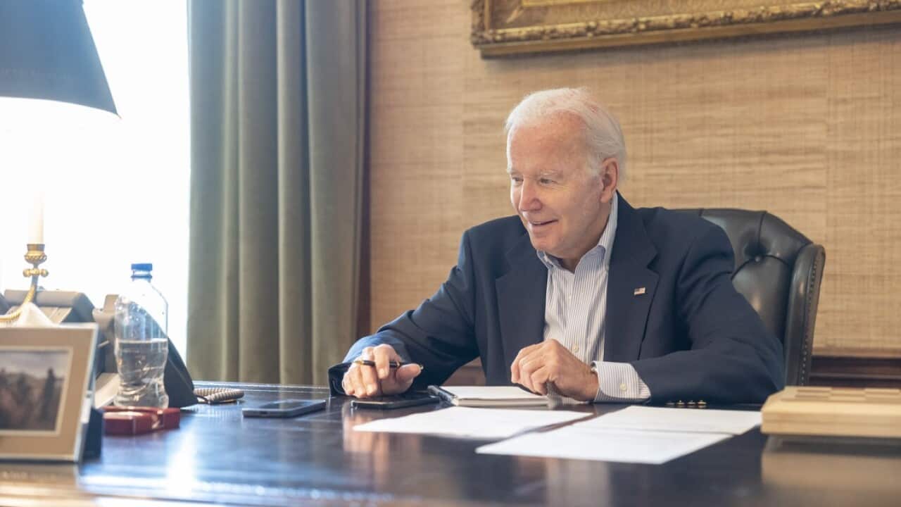 A smiling Joe Biden is seated at a desk.