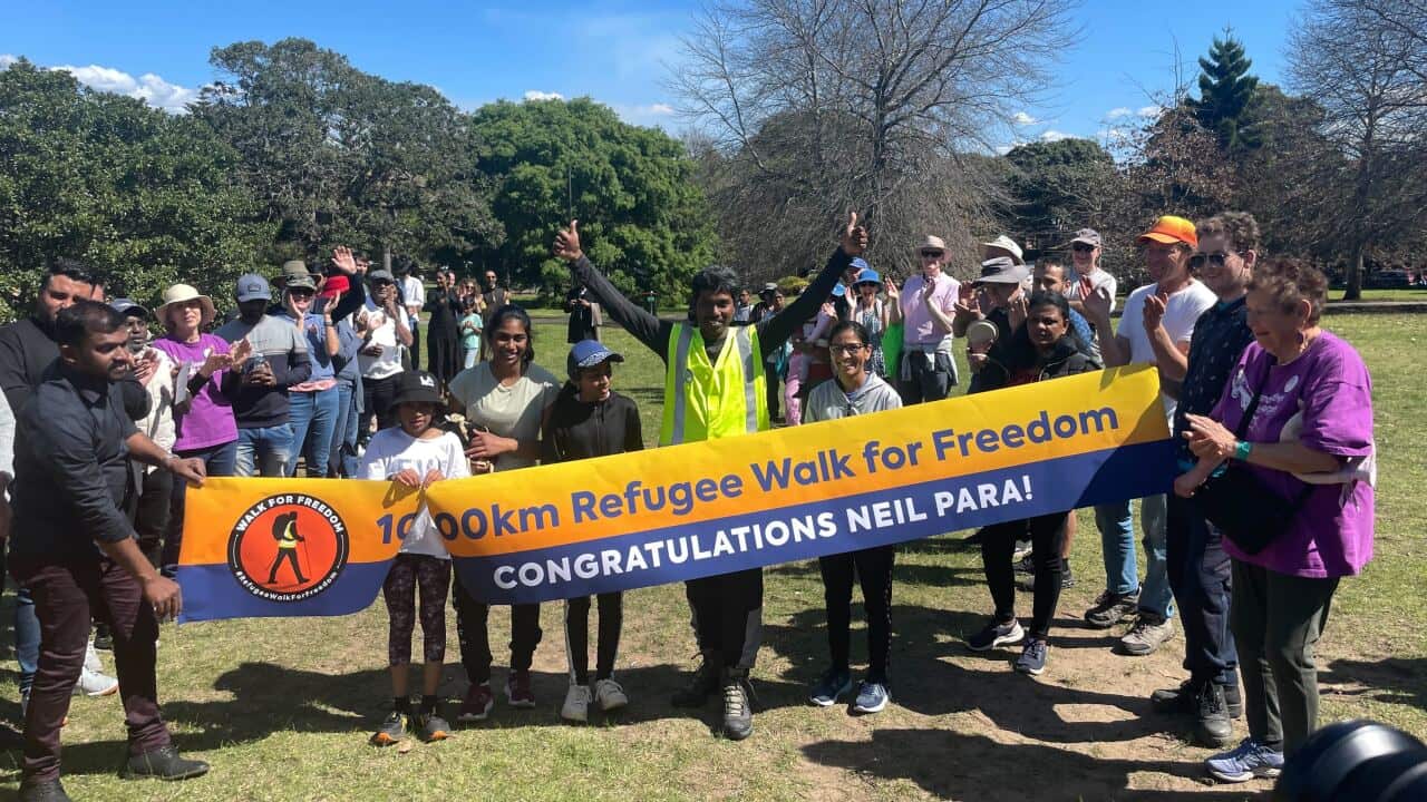 A man in a high-vis vest with arms raised in celebration surrounded by a group of people holding a banner.