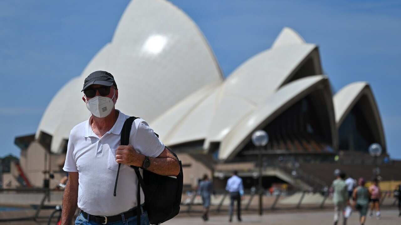 People wearing masks walk in front of the Sydney Opera House.