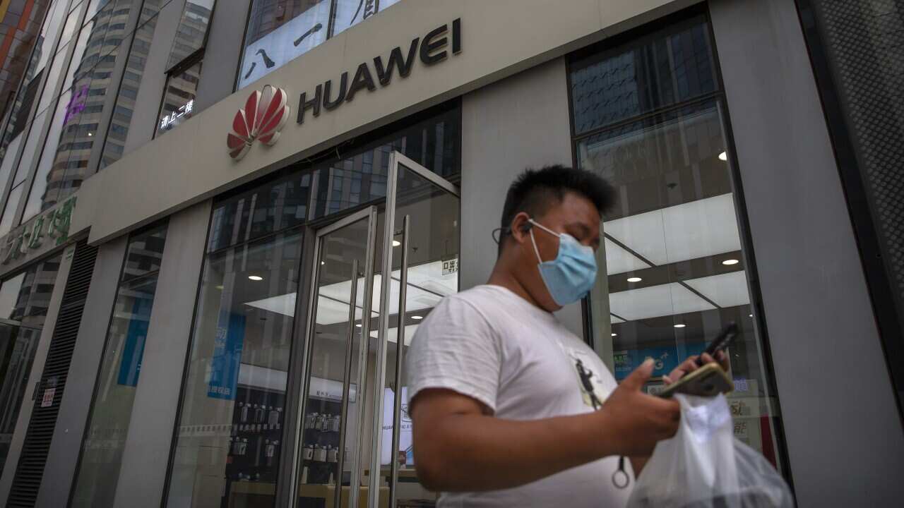A man wearing a face mask to protect against the new coronavirus looks at his smartphone as he walks past a Huawei store in Beijing.