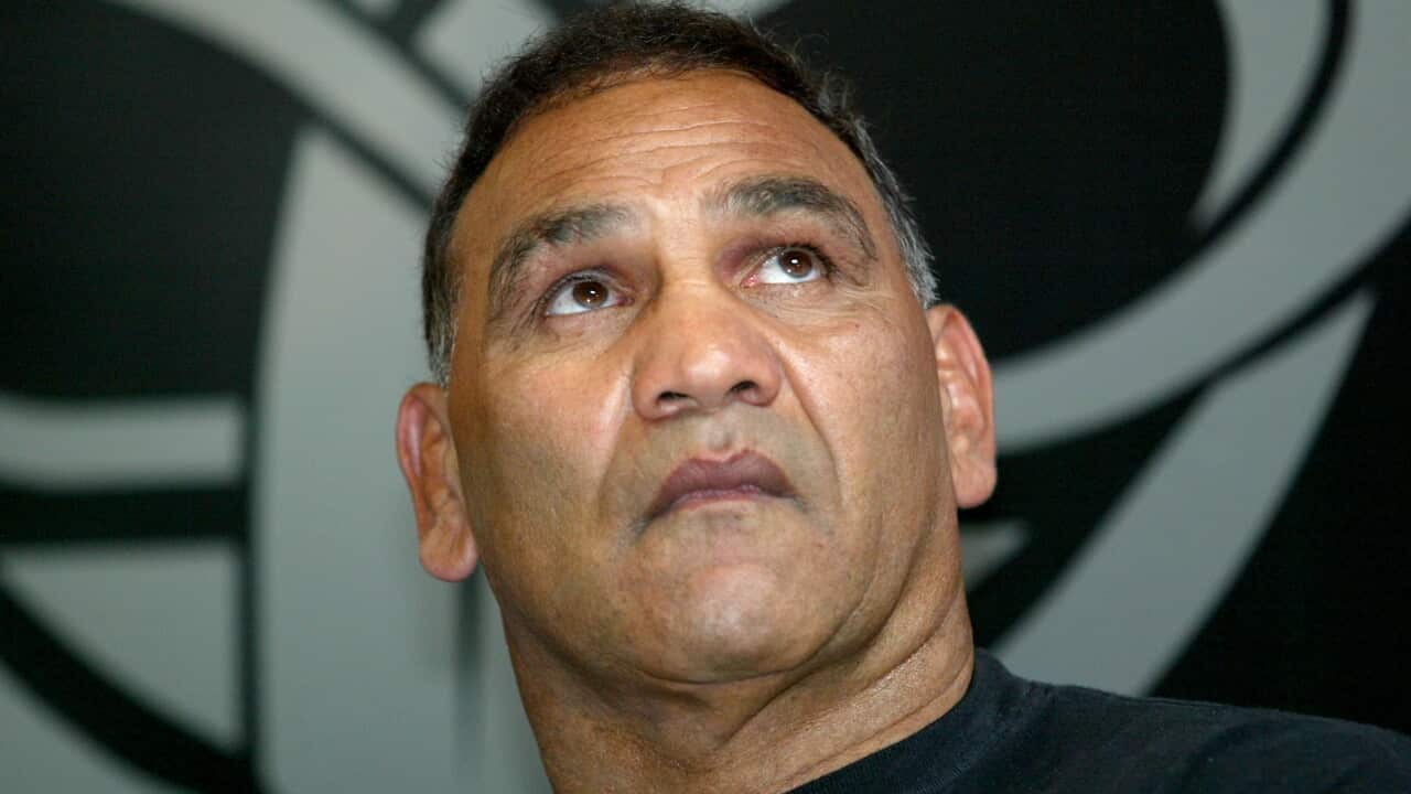 Close-up portrait of a man in a dark shirt looking upward, with a large black-and-white graphic design visible in the background.