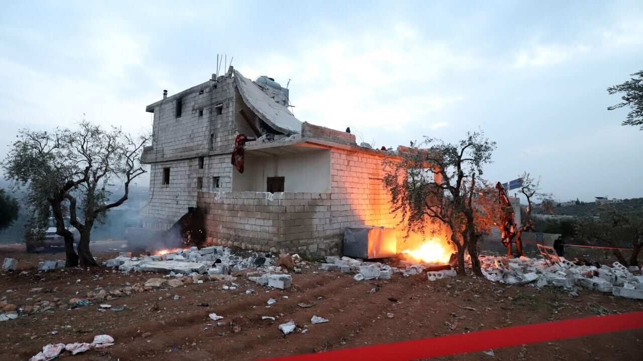 Red tape is extended and objects are set on fire, around the hous in which the leader of Islamic State (IS) group Amir Mohammed Said Abd al-Rahman al-Mawla died, during an overnight raid by US special forces, in the town of Atme in Syria's northwestern pr