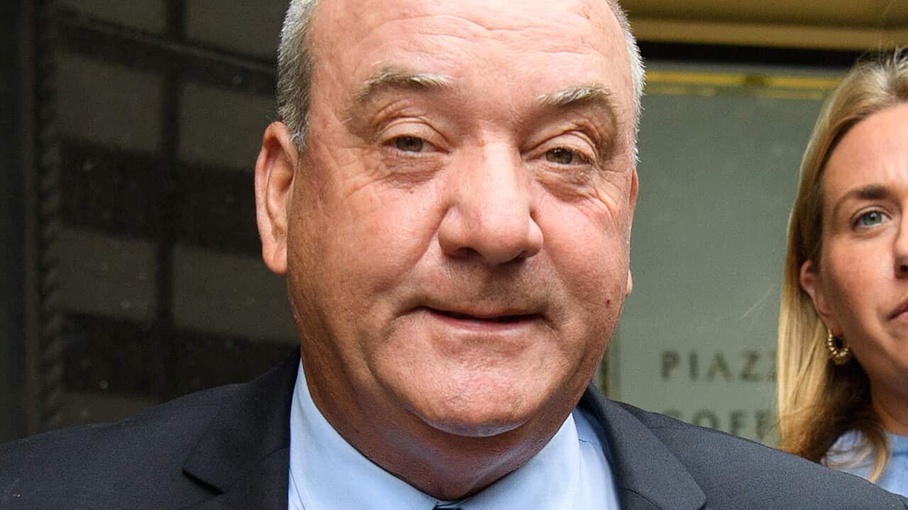 A man in a black suit, blue shirt and blue tie.