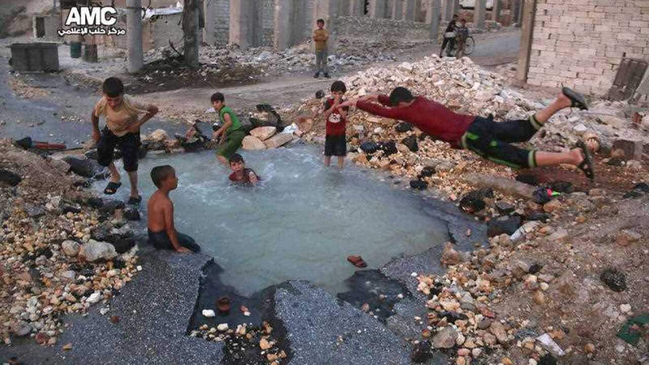 Syrian boys dive into a hole filled with water that was caused by a missile attack in the rebel-held neighborhood of Sheikh Saeed in Aleppo