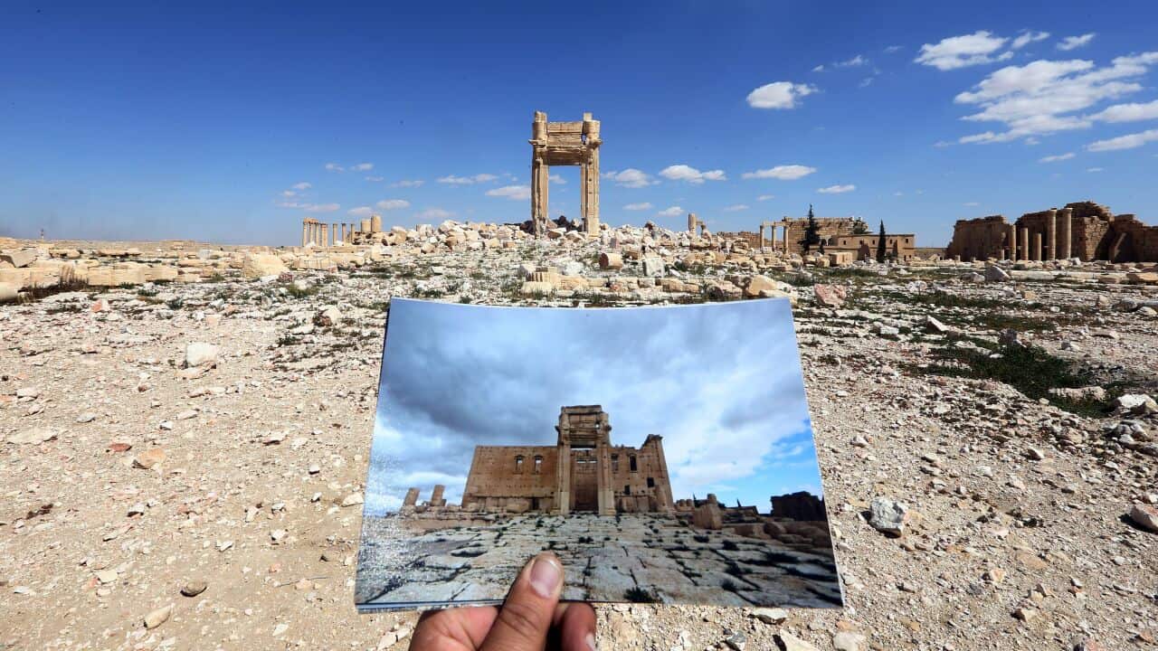 A general view taken on March 31, 2016 shows a photographer holding his picture of the Temple of Bel taken on March 14, 2014 in front of the remains of the historic temple after it was destroyed by Islamic State (IS) group jihadists in September 2015 in t