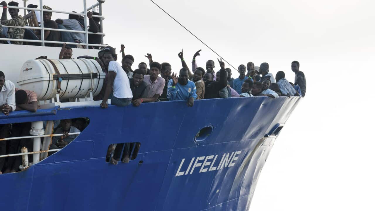 Migrants wave from aboard a ship operated by the German NGO Mission Lifeline.