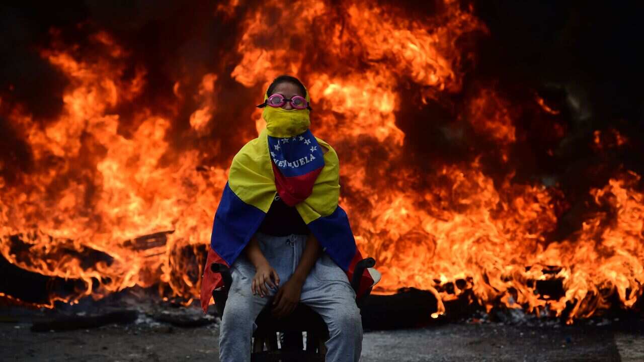 A Venezuelan opposition activist is backdropped by a burning barricade during a demonstration against President Nicolas Maduro in Caracas, on April 24, 2017.Protesters rallied on Monday vowing to block Venezuela's main roads to raise pressure on Maduro af