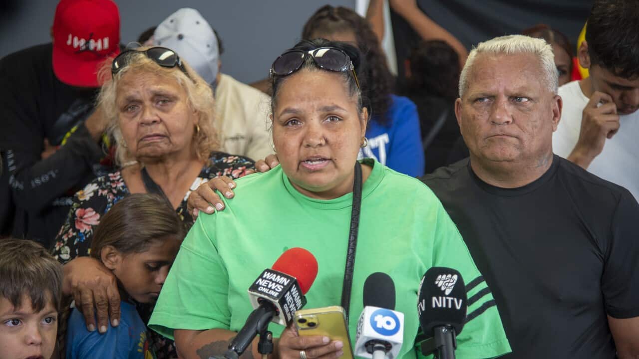 A noongar woman speaks into press microphones, surrounded by family and supporters.