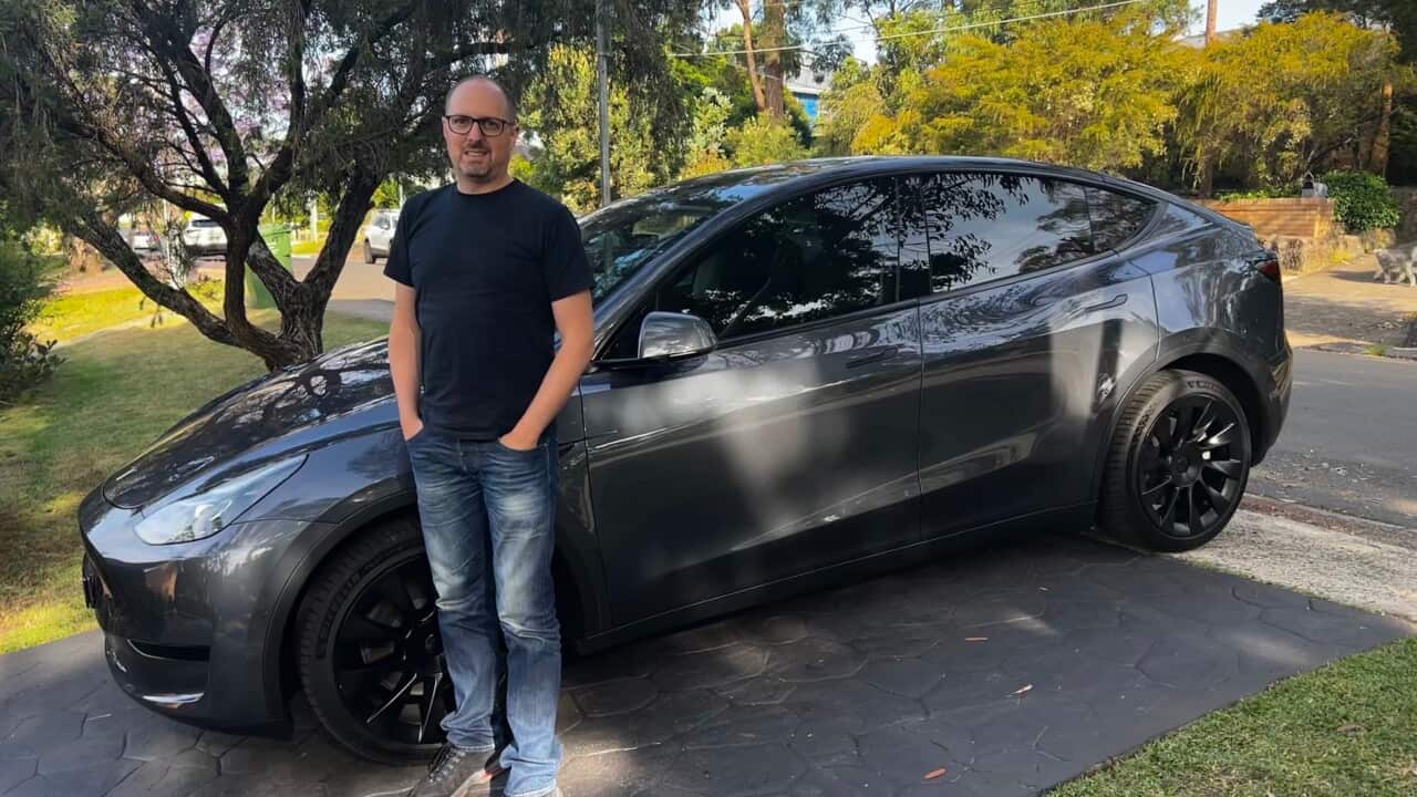 A man standing outside next to a car parked in a driveway.
