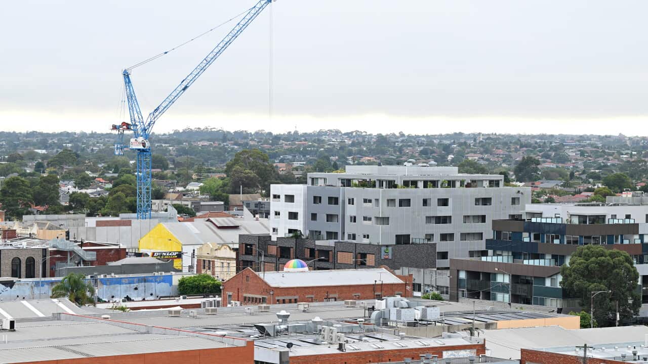Construction crane towers above apartment and commercial buildings in a suburban Melbourne streetscape.