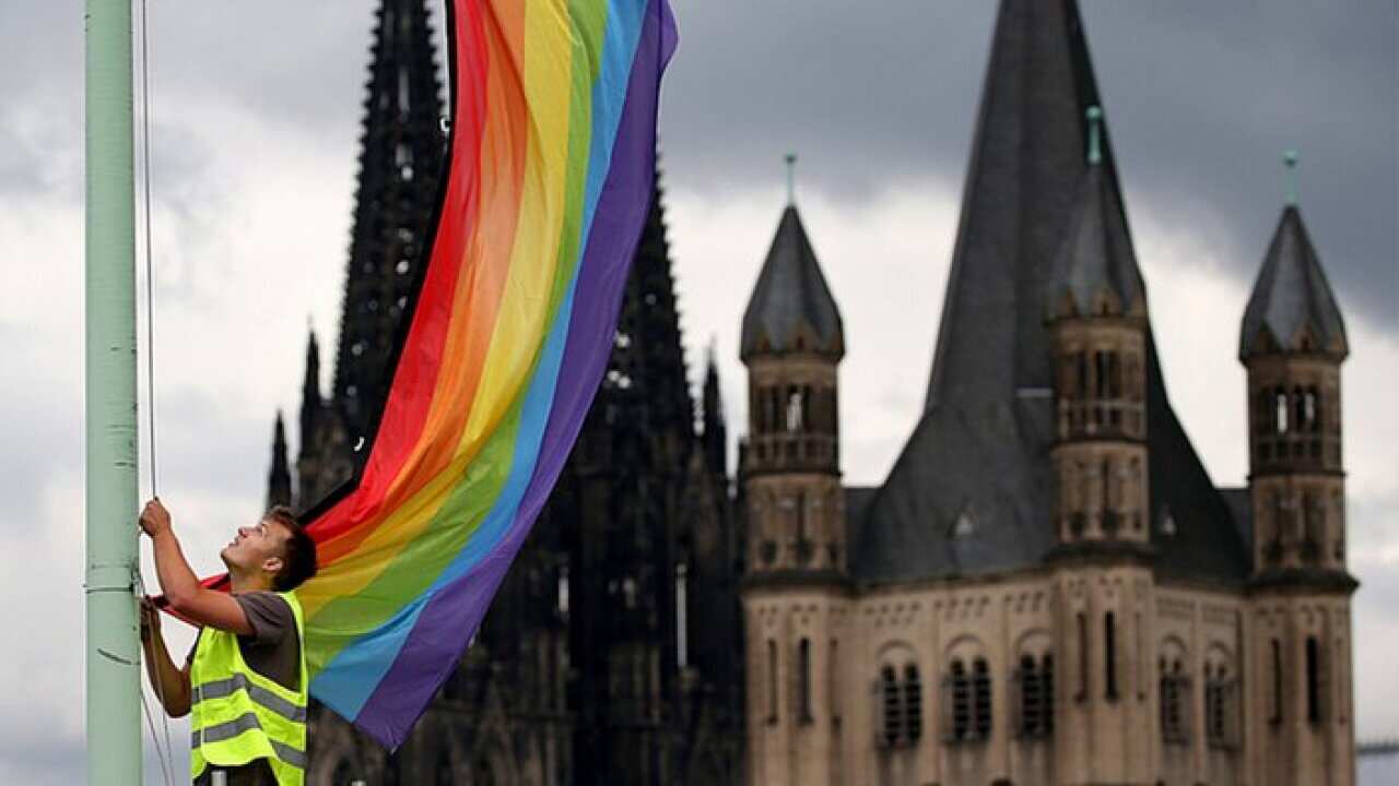 A rainbow flag being hung in front of a church in Germany