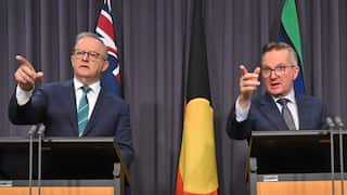 Energy Minister Chris Bowen standing at lecterns alongside Prime Minister Anthony Albanese, both are pointing