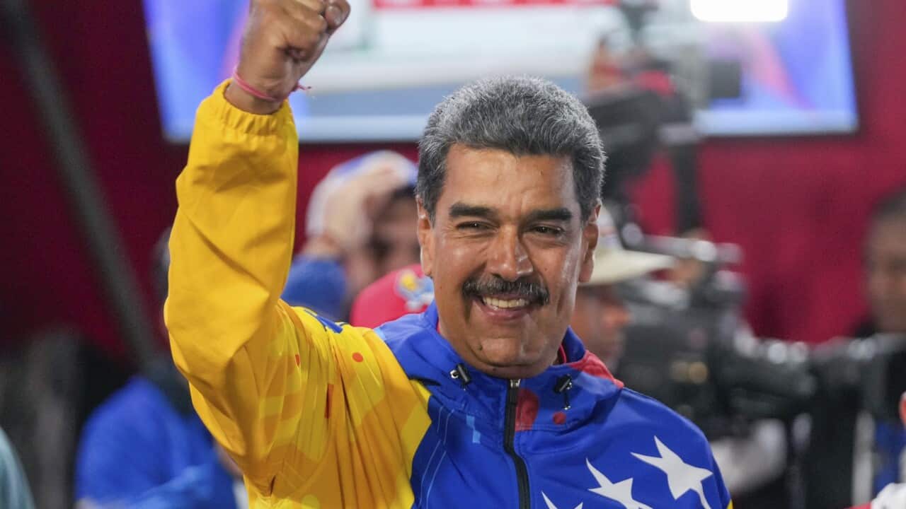 Nicolas Maduro raising his hand and smiling while wearing a brightly-coloured jacket.