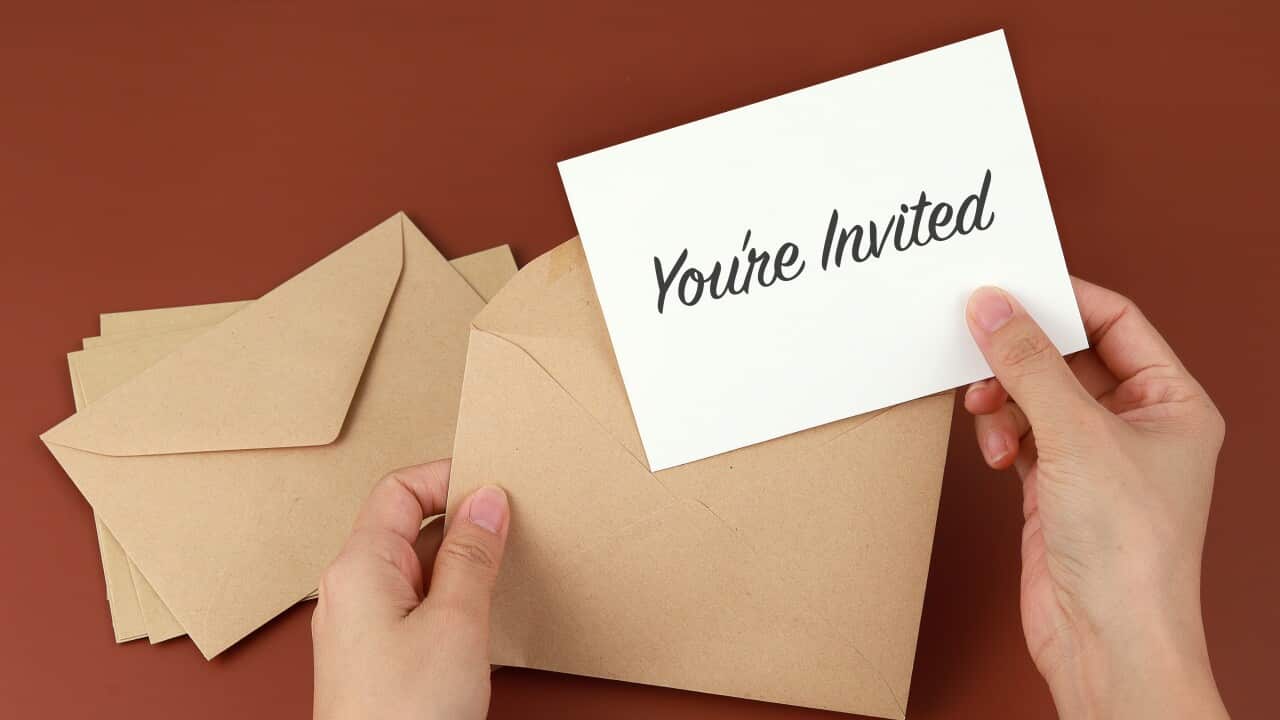 Cropped Hands Of Woman Holding Invitation Card On Brown Background