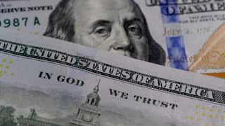 Close-up of overlapping U.S. currency, showing Benjamin Franklin’s face on a $100 bill partially covered by another bill, with visible text including “United States of America” and “In God We Trust".