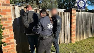 Police arresting a man against a fence.