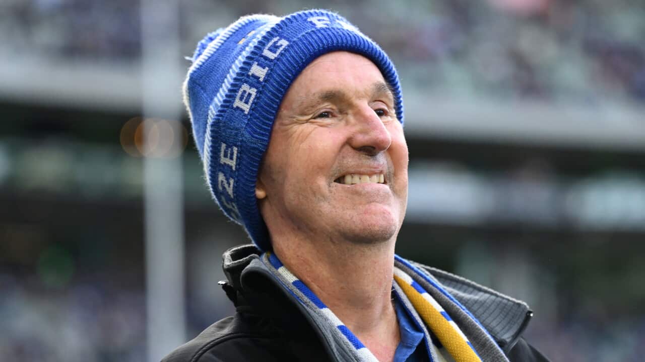 An older man in a blue beanie and scarf smiles
