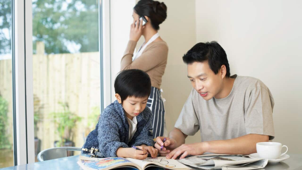 Father and Son coloring in Coloring Book on table mother talking on mobile