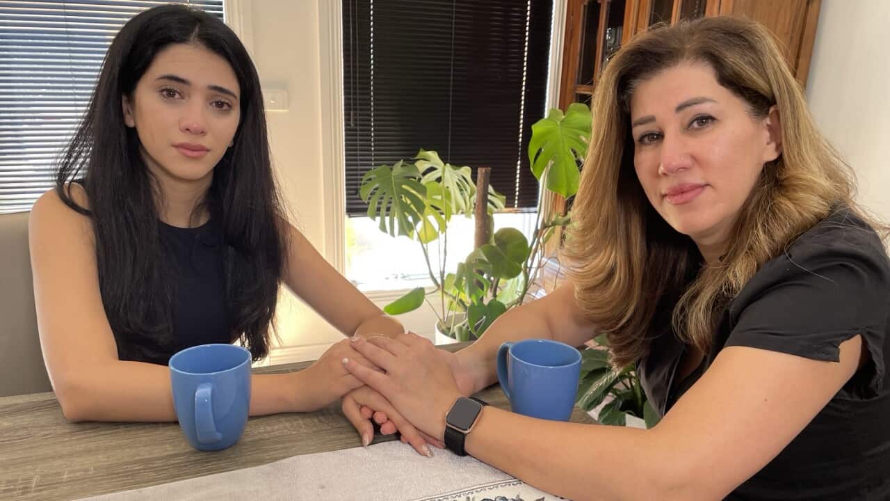 A mother and daughter hold hands while sitting at a table.
