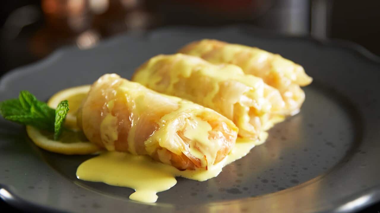 Three cabbage rolls, drizzled wth a yellow sauce, sit on a round dull silver tray.