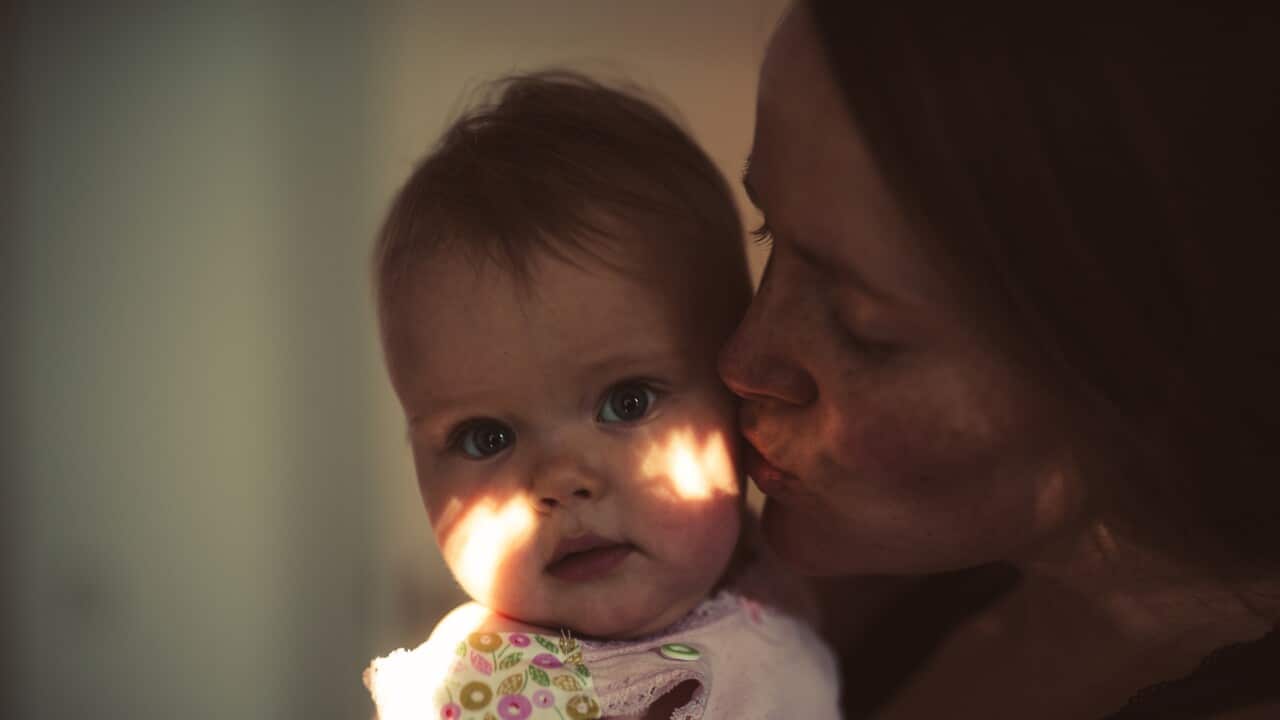Happy mother kissing her smiling baby girl at home.