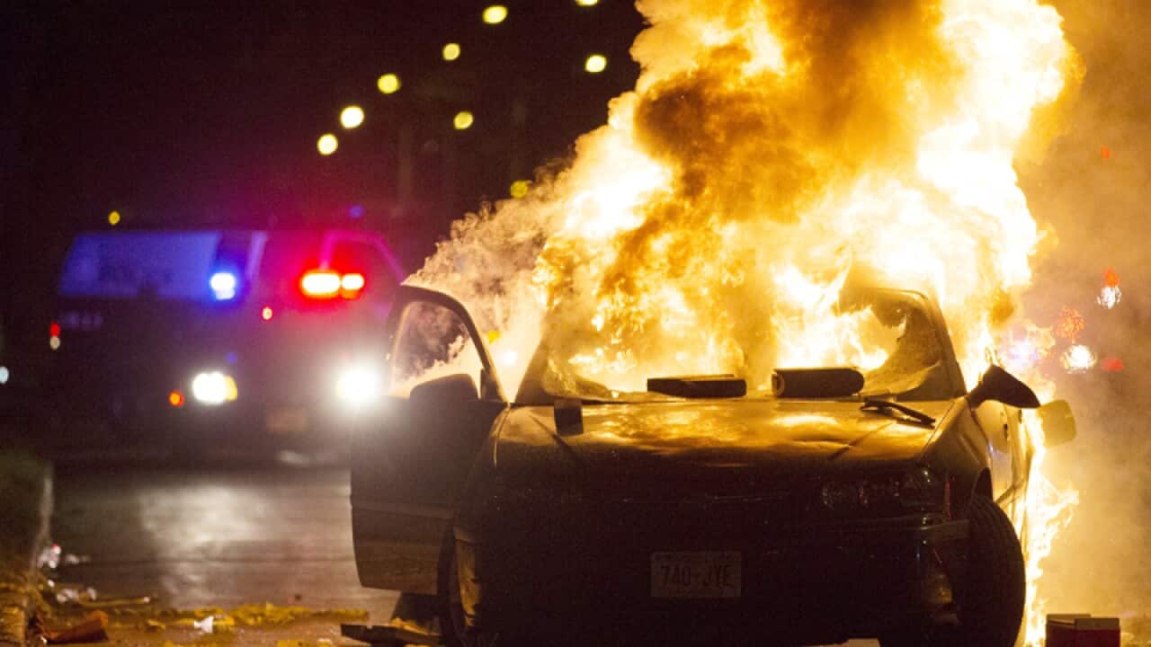 A car burns as a crowd of more than 100 people gathers