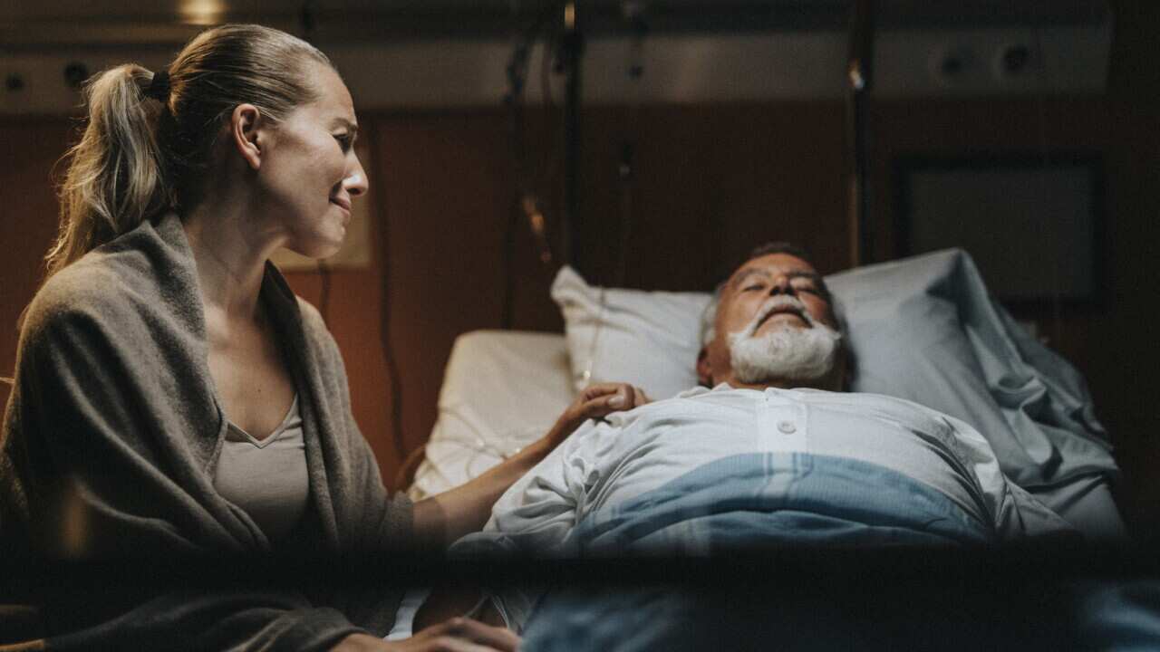 Depressed mature daughter crying near father in hospital ward
