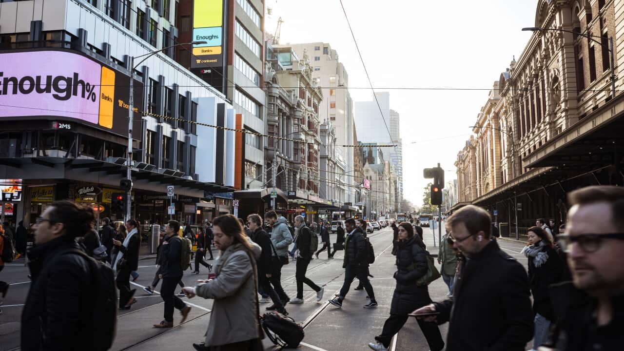 Pedestrians cross a busy city intersection lined with shops and office buildings in Melbourne's CBD.