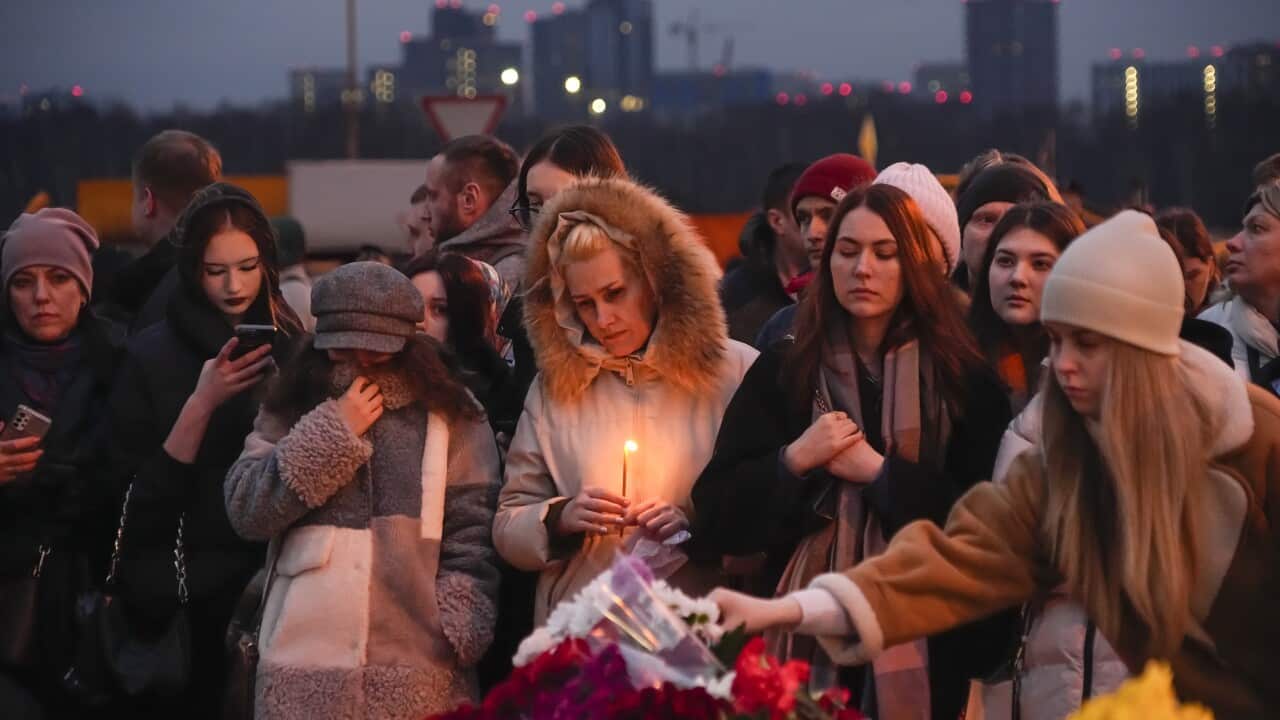 Women dressed in winter coats laying flowers at a memorial