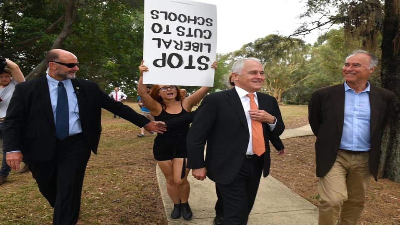 A protester confronts Malcolm Turnbull and John Alexander.