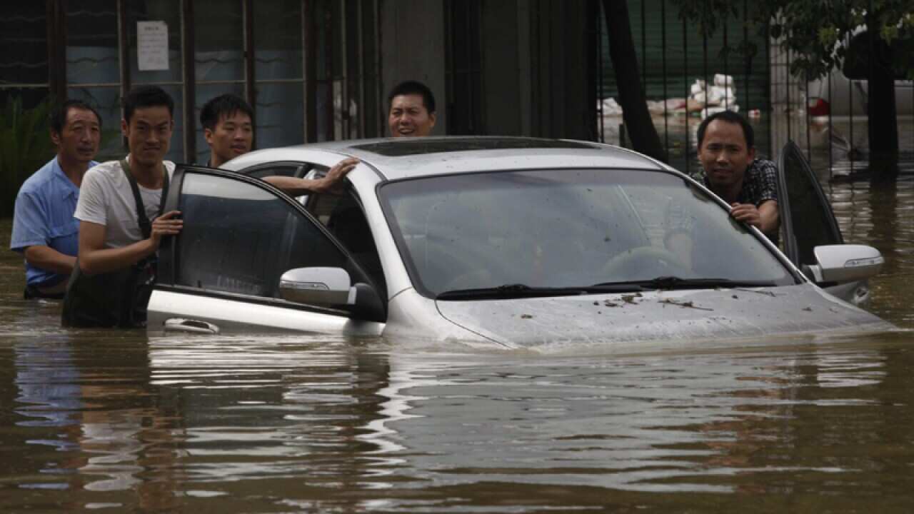 Workers try to push a vehicle trapped on a flooded street