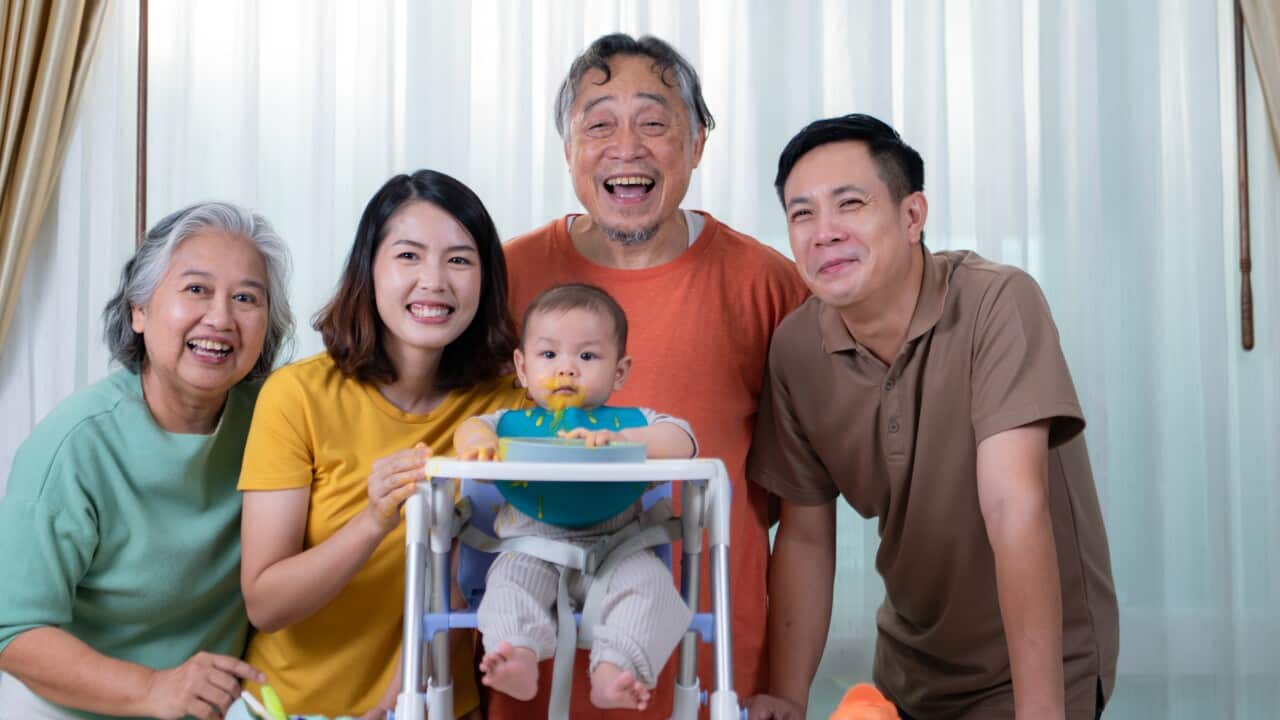 A little child eating his first meal, parents and grandparents c