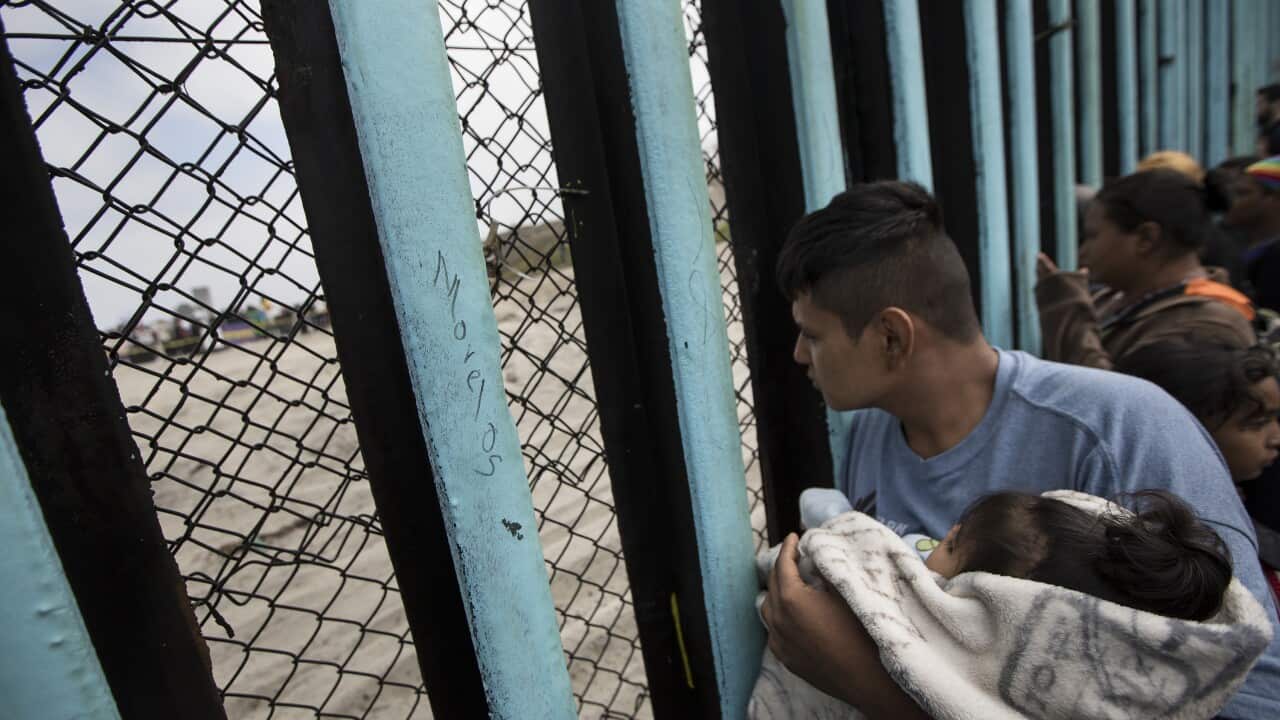 A member of the Central American migrant caravan, holding a child, looks through the border wall toward a group of people gathered on the U side, as he stands on the beach where the border wall ends in the ocean, in Tijuana, Mexico