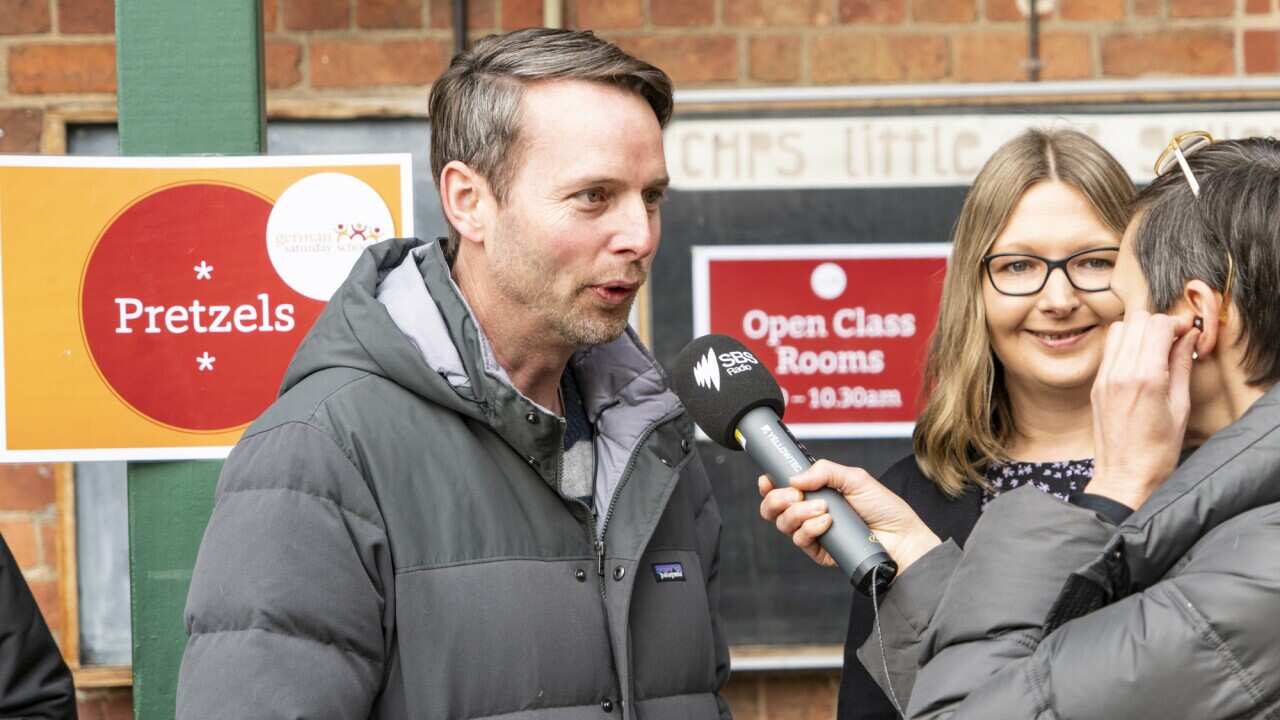 A man speaks into an SBS microphone while a smiling woman looks on.