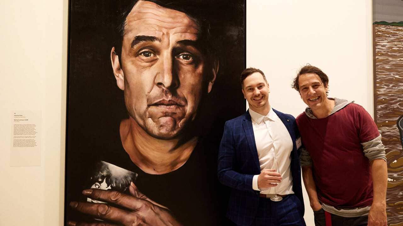 An artist and his subject pose against an artwork.