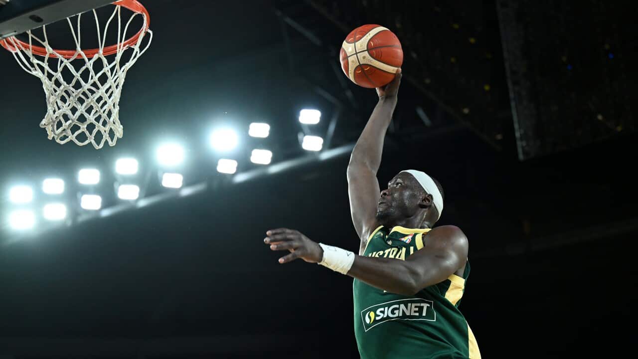 A man in mid-air holding a basketball in one hand with a basketball hoop on the left.