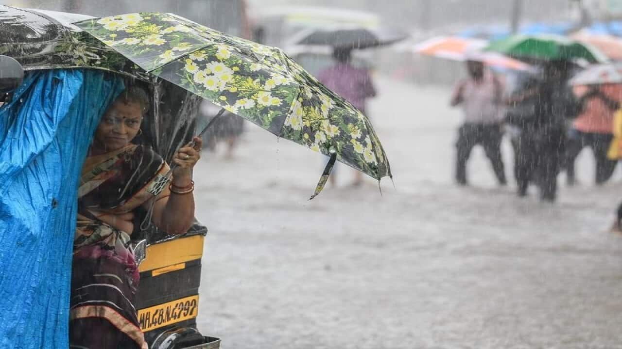 Indian people cover themselves under umbrellas in a flooded street.