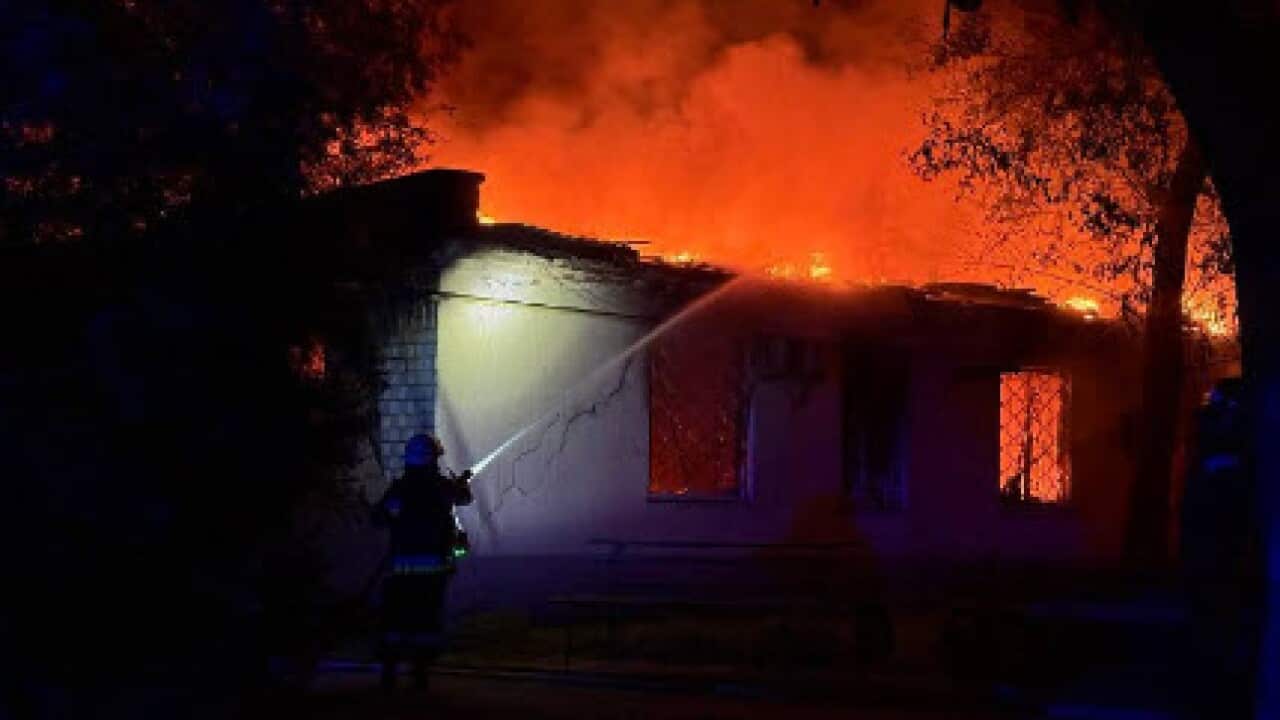 A firefighter uses a hose to douse plumes of smoke rising from a burning building.