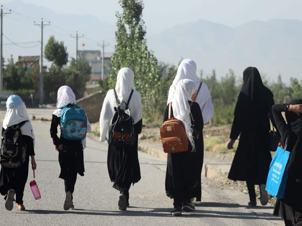 A group of girls wearing headscarves and backpacks walk on a road to school