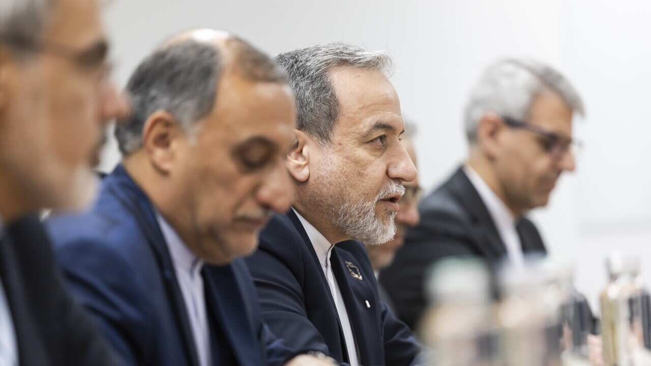 Men in suits sit at a table facing in one direction.