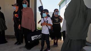 Members of a family with baggage wait between two buildings.