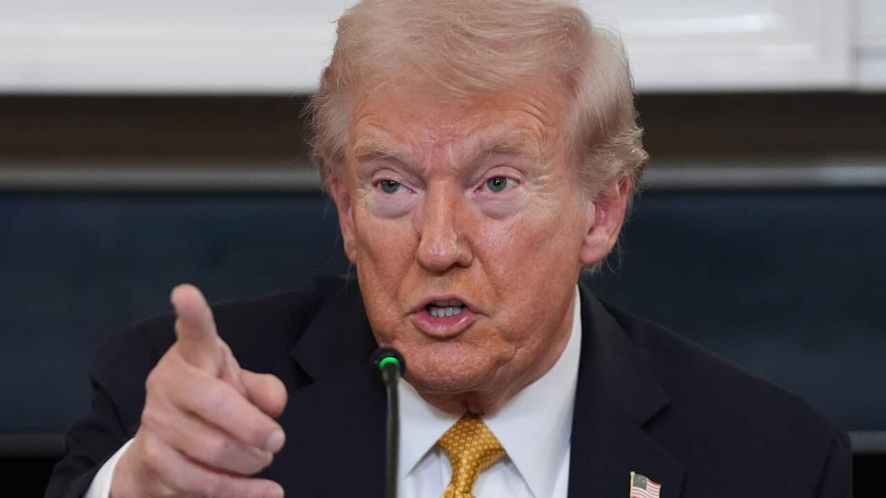 Donald Trump, in a dark suit and a yellow tie, is pointing with his finger as he speaks.
