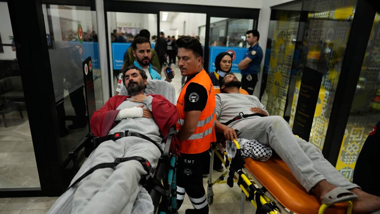 Two patients on stretchers are wheeled through a busy indoor facility by medical personnel and emergency responders.